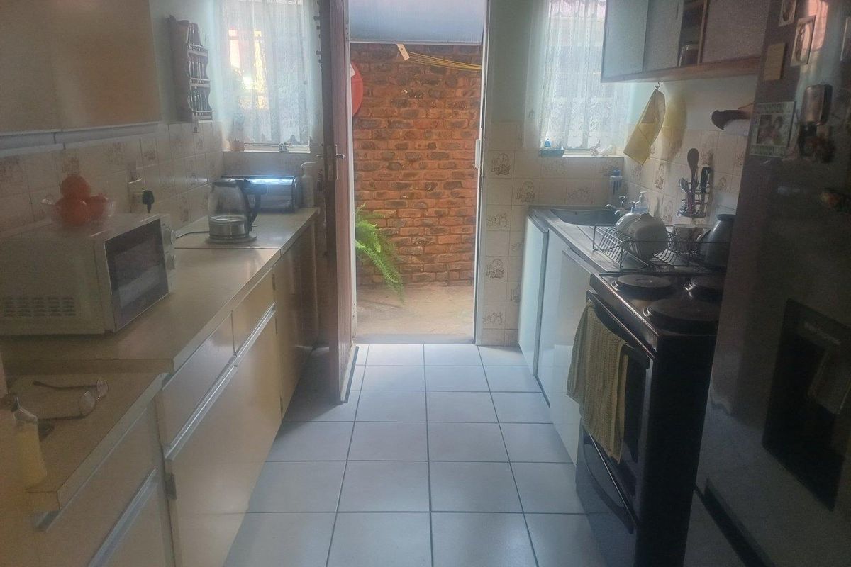 A functional galley-style kitchen featuring tiled flooring, built-in cabinetry, and a freestanding stove, with direct access to an outdoor rear area.