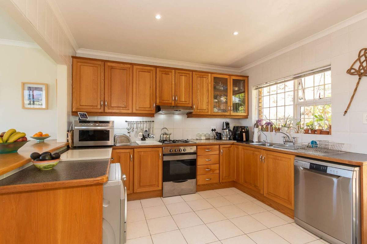A functional kitchen featuring wooden cabinetry, tiled flooring, a built-in oven with gas hob, and a double sink with a window view.