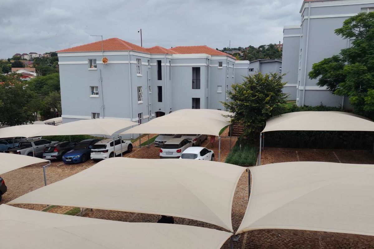 Exterior view of an apartment complex featuring a paved parking area with multiple shade sail carports and multi-story residential buildings.