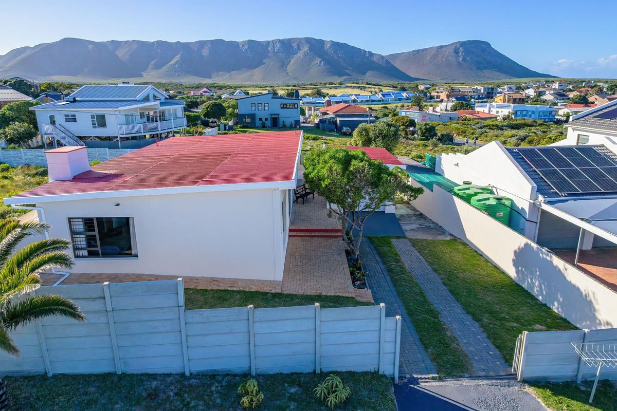 Aerial view of the property featuring a red metal roof, paved driveway, and boundary wall, set against a scenic mountain backdrop.