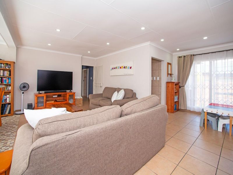 A bright and spacious living room featuring neutral tiled flooring, recessed downlighting, and a sliding glass door leading to the exterior.