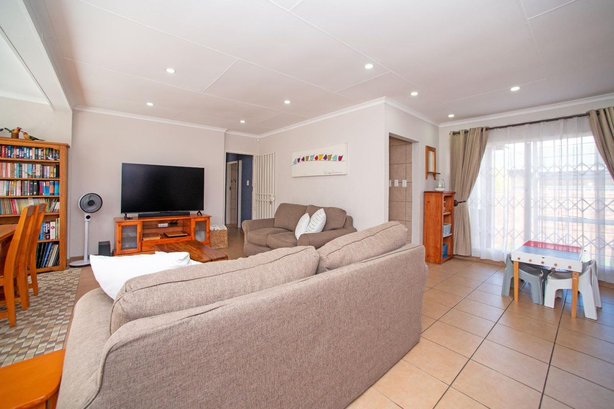 A bright and spacious living room featuring neutral tiled flooring, recessed downlighting, and a sliding glass door leading to the exterior.