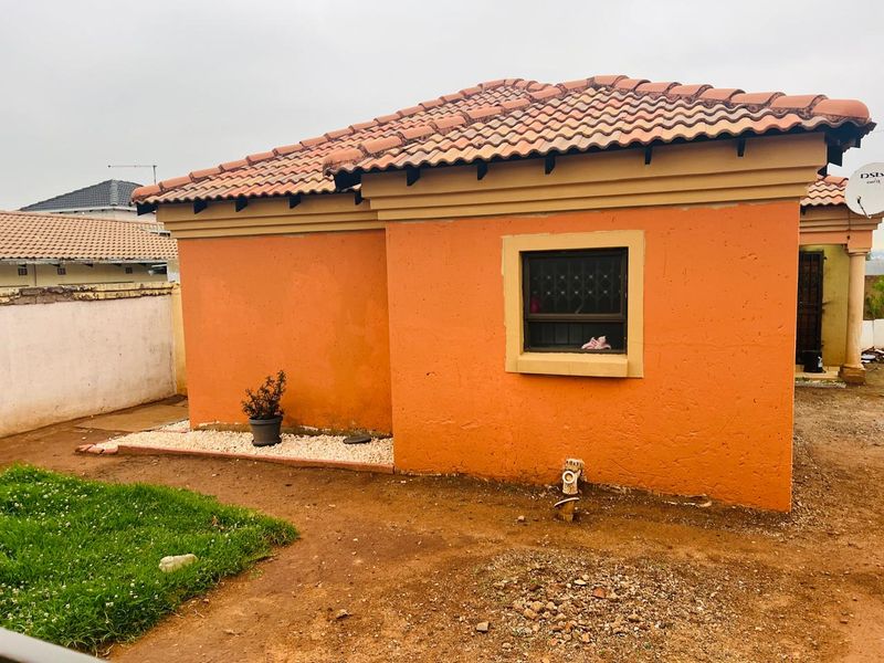 Rear view of a single-story house featuring terracotta roof tiles, orange exterior walls, and security bars on the window.