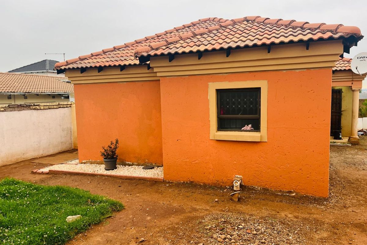 Rear view of a single-story house featuring terracotta roof tiles, orange exterior walls, and security bars on the window.