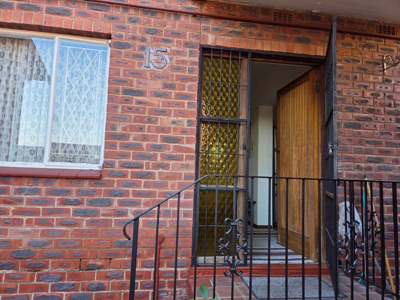 Front entrance of a townhouse featuring a classic face brick facade, secure wrought iron gate, and a solid timber front door.