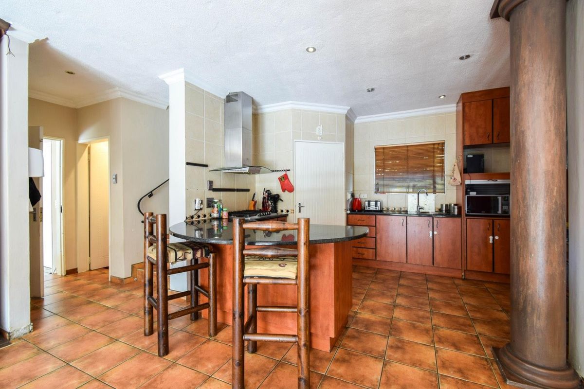 A functional kitchen featuring wooden cabinetry, granite countertops, a central breakfast island, and a stainless steel extractor fan.