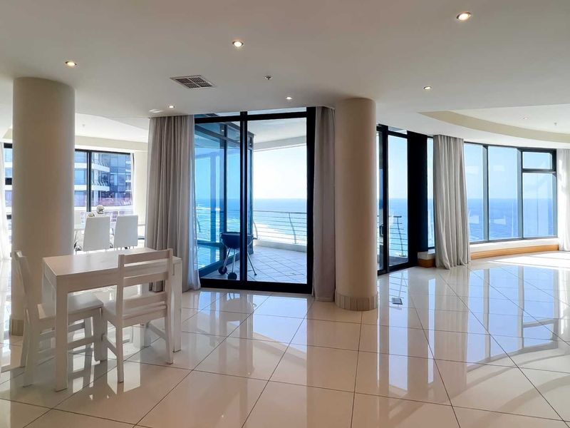 Spacious open-plan living area featuring large floor-to-ceiling windows, polished tile flooring, recessed lighting, and direct access to a private balcony with ocean views.
