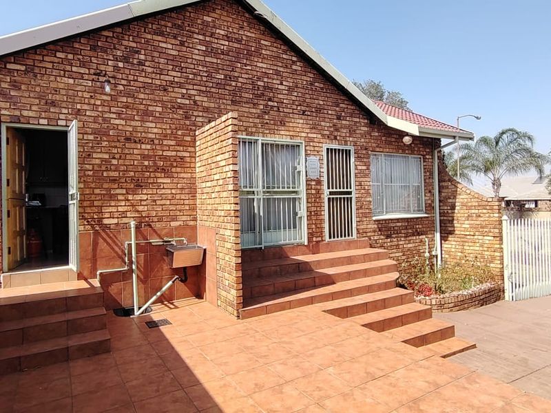 Rear exterior view of the house featuring a face brick facade, tiled patio area, security gates, and an external wash basin.