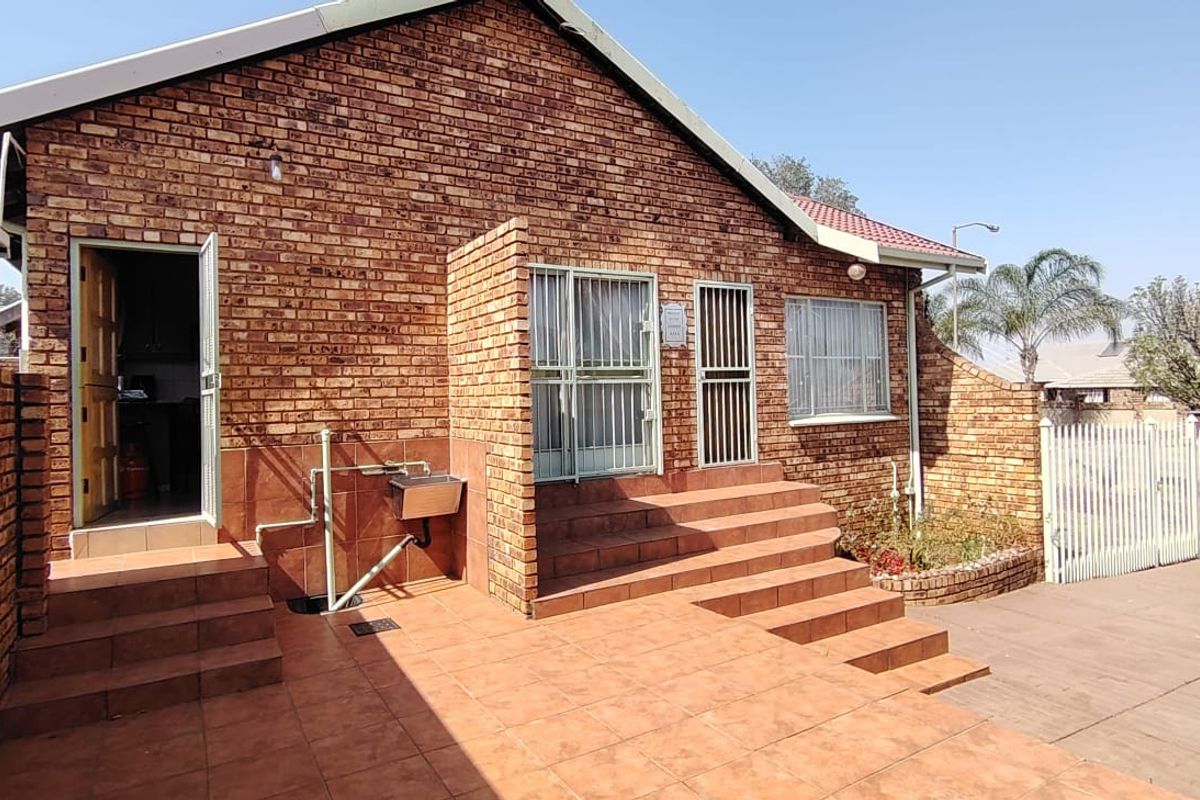Rear exterior view of the house featuring a face brick facade, tiled patio area, security gates, and an external wash basin.