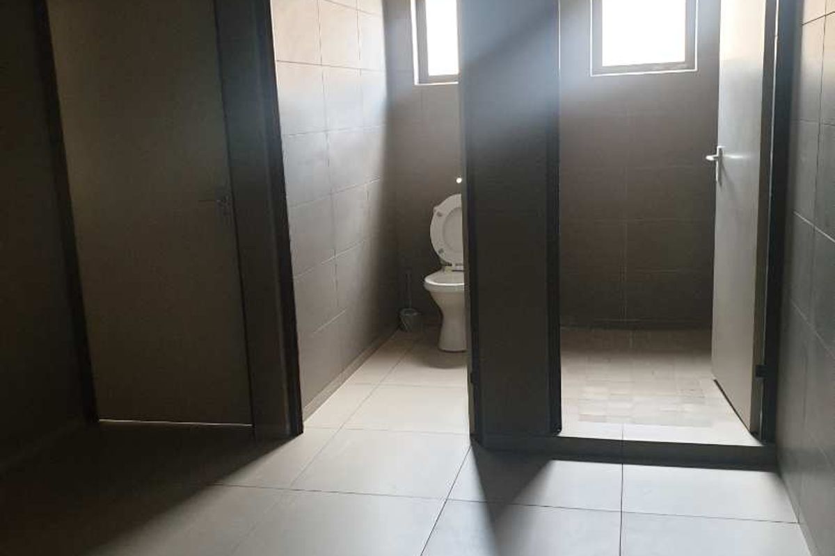 A functional industrial restroom area featuring tiled flooring, multiple doorways, and a private toilet cubicle with natural light.
