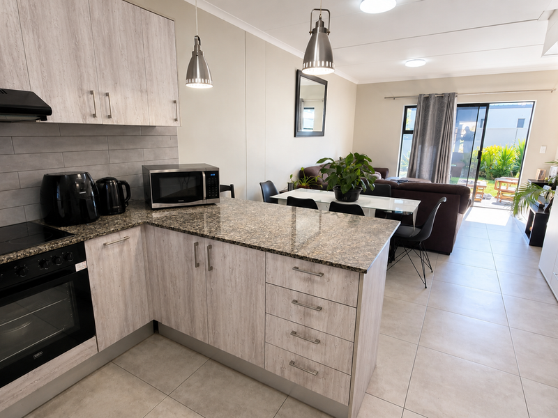 Modern open-plan kitchen and living area featuring light wood-grain cabinetry, granite countertops, tiled floors, and direct access to the rear patio.