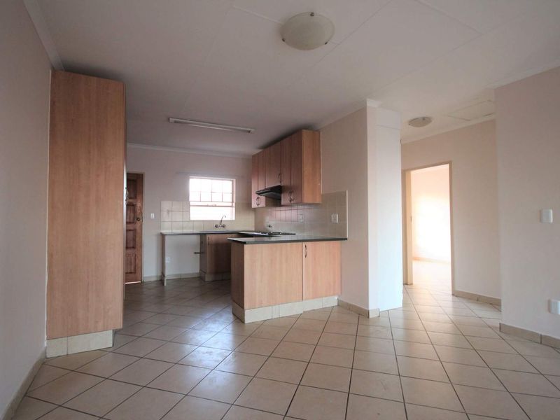 An open-plan kitchen and living area featuring tiled flooring, built-in wooden cabinetry, and a functional layout with a breakfast counter.