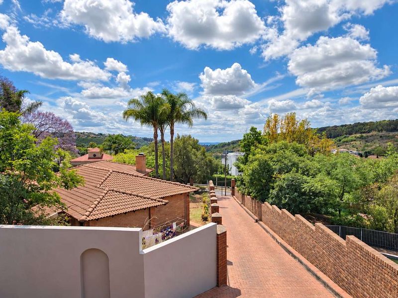 Elevated view overlooking the property grounds, featuring a brick driveway, boundary walls, and surrounding lush landscape with a clear sky.