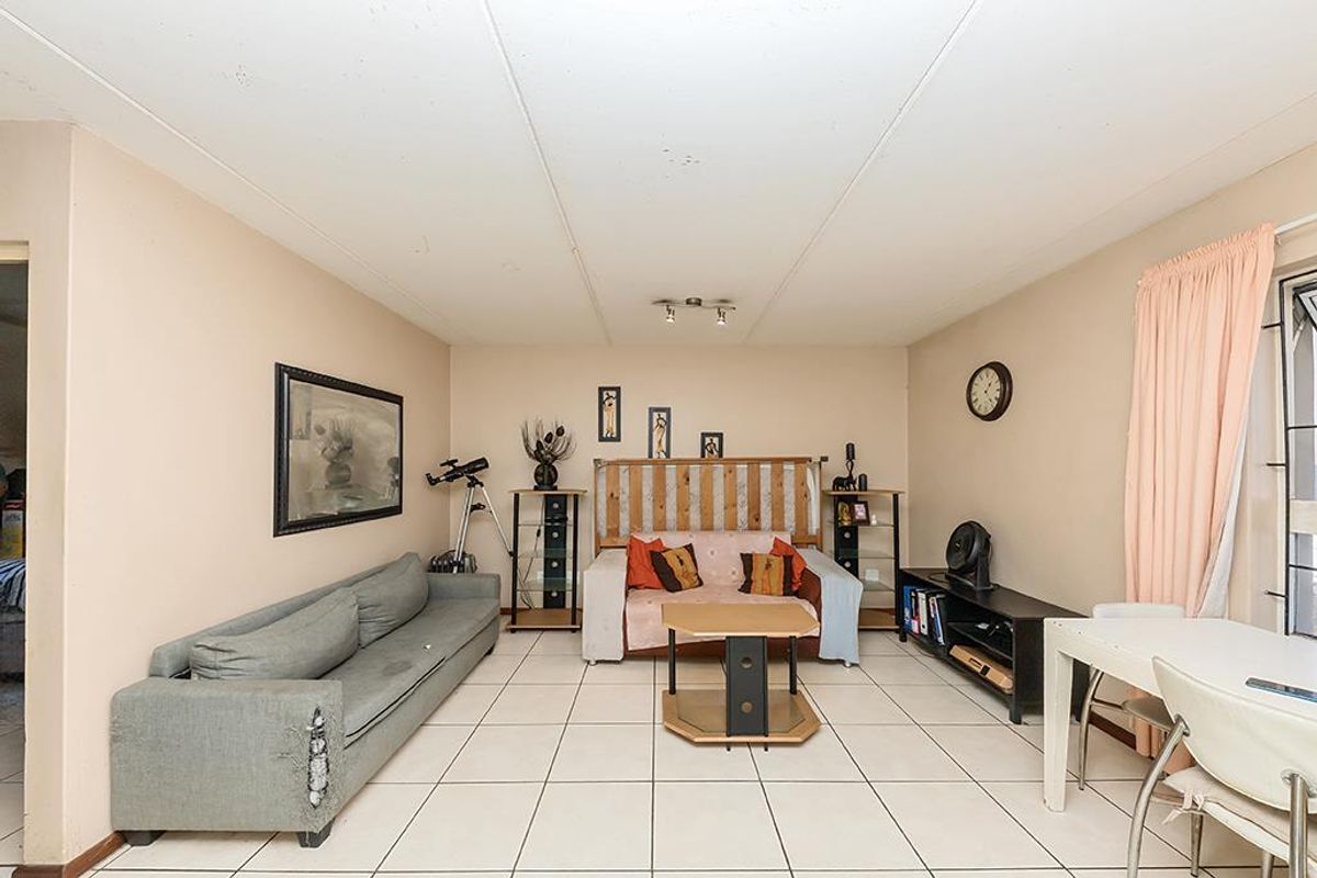 A living room featuring tiled flooring and ceiling-mounted spotlights, currently showing signs of wear on the walls and ceiling.