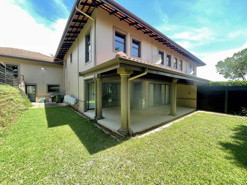 Rear view of the townhouse featuring a spacious covered patio with classic columns, tiled roof, and access to a private garden area.