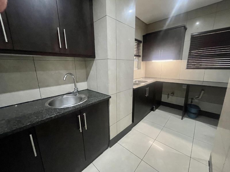 A functional kitchen featuring dark wood cabinetry, granite countertops, stainless steel sink, and tiled finishes throughout.