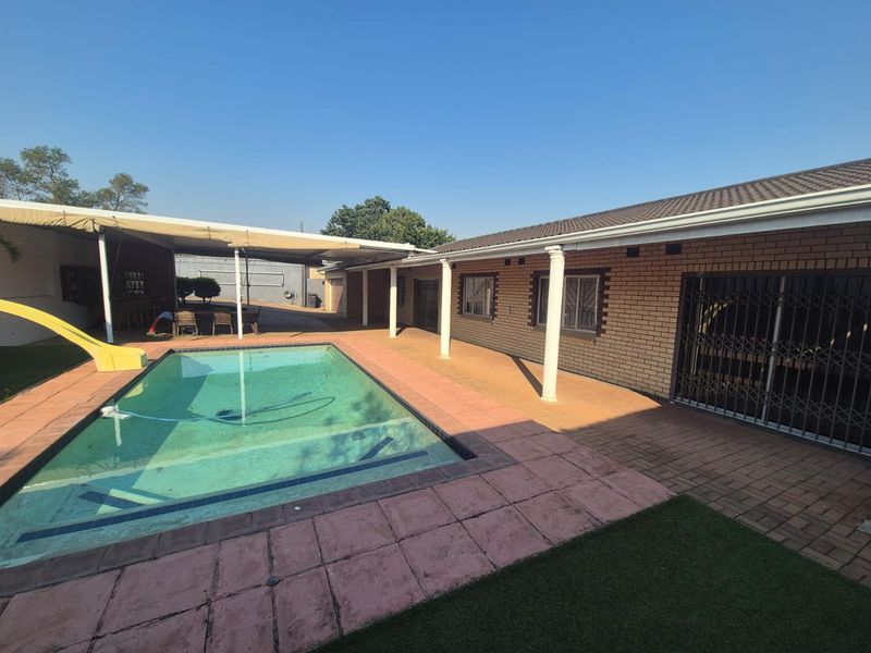 Outdoor pool area featuring a paved deck, covered patio space, and brick exterior facade with security gates.