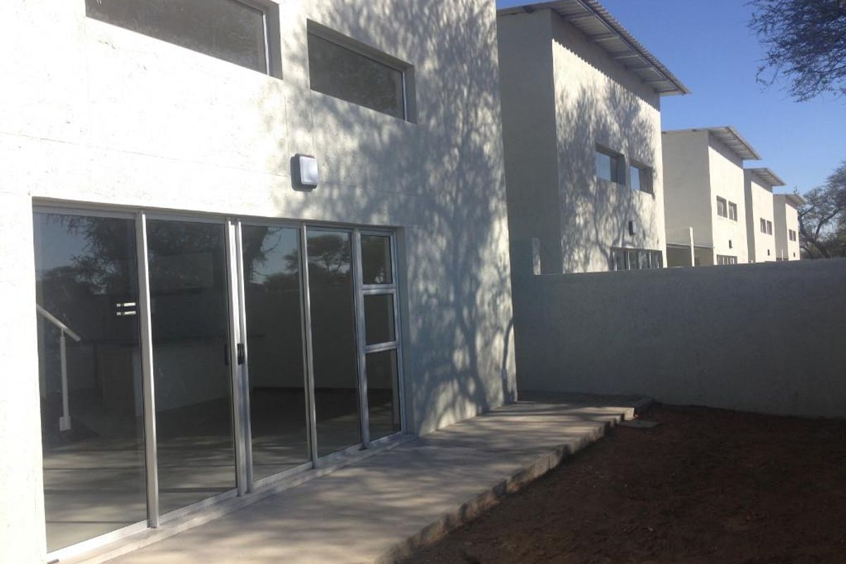 Rear view of a modern townhouse featuring a concrete patio, large sliding glass doors, and a private backyard area.