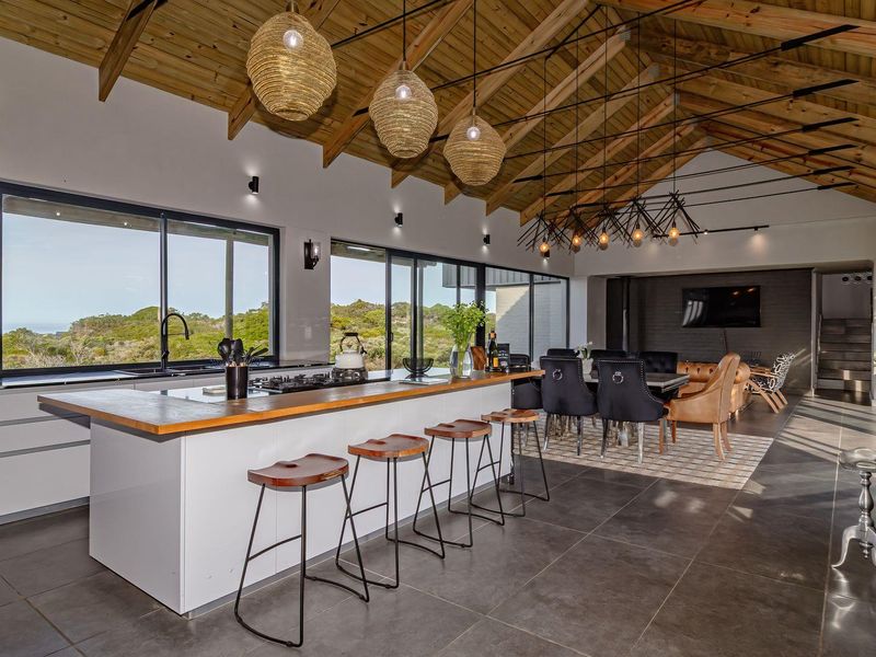 Spacious open-plan kitchen and living area featuring a high exposed timber truss ceiling, modern kitchen island, and large sliding doors with scenic views.
