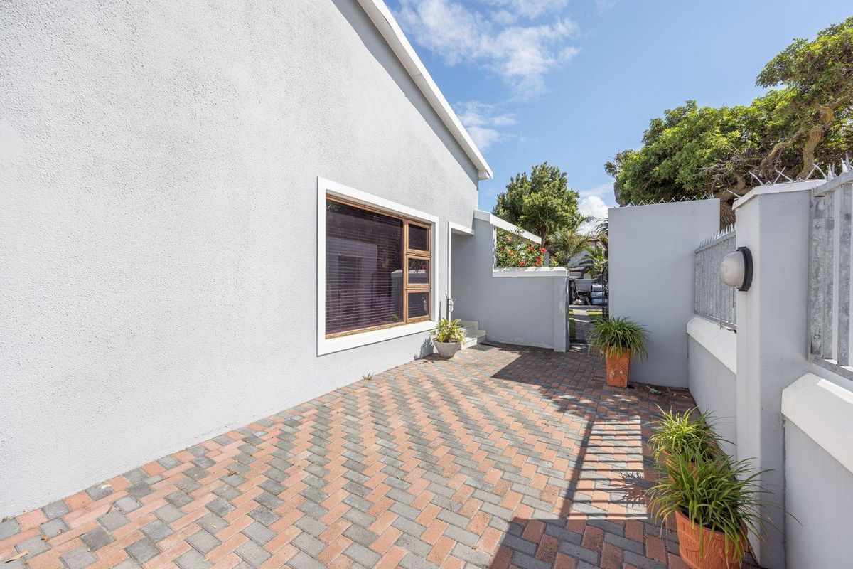 A paved rear courtyard area featuring a rendered exterior wall, secure boundary fencing with spikes, and a timber-framed window.