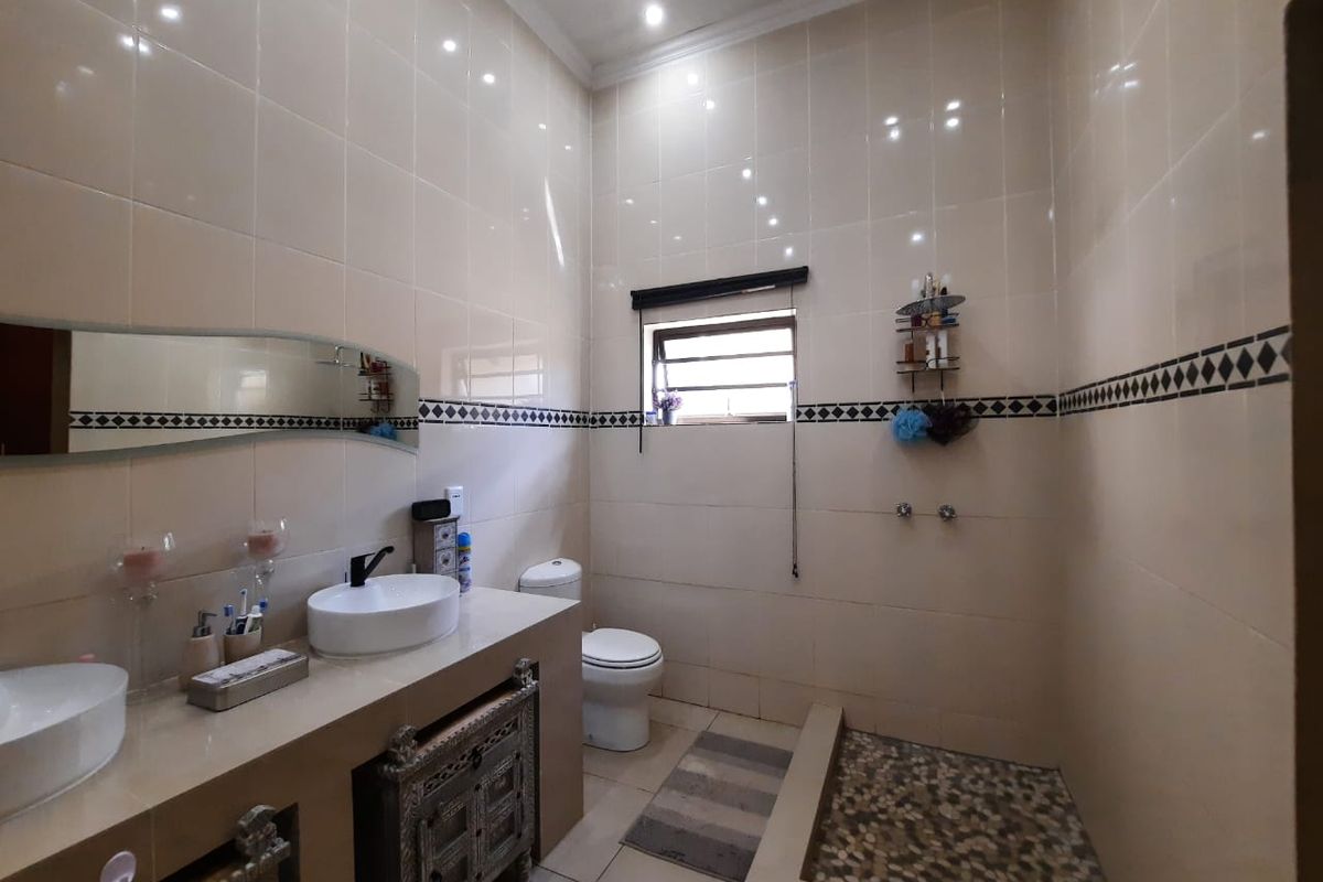 A functional bathroom featuring a double vanity with vessel sinks, a walk-in shower with pebble flooring, and full-height wall tiling.
