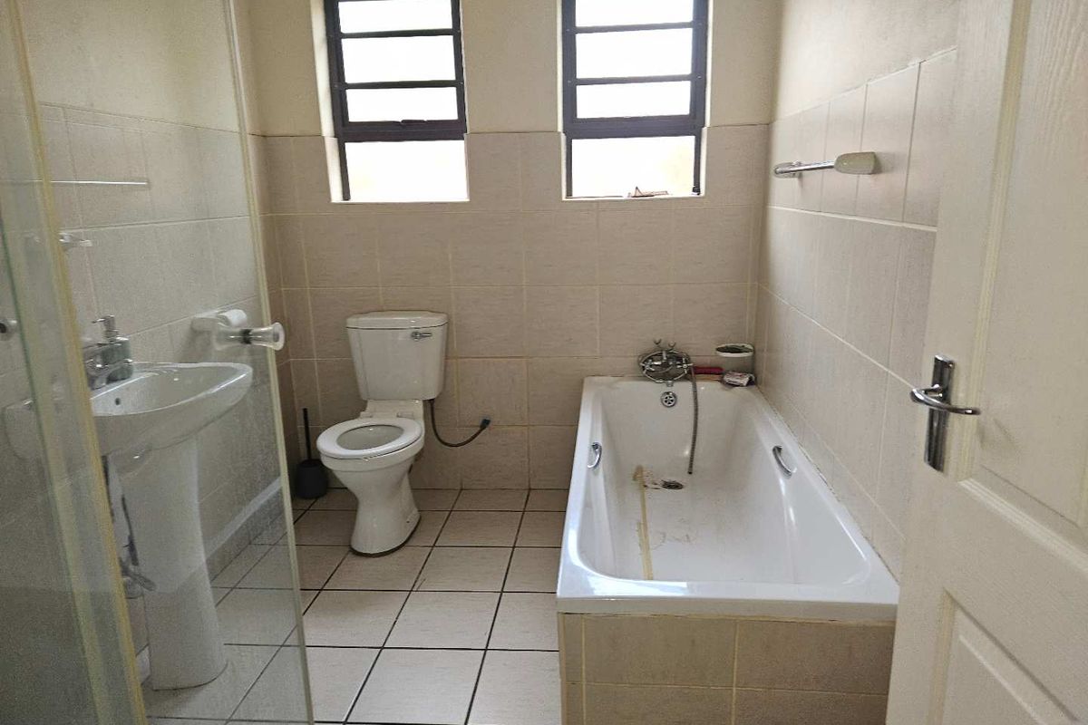 A functional bathroom featuring a pedestal basin, toilet, and bathtub with tiled finishes, requiring some cosmetic updates to restore its appeal.