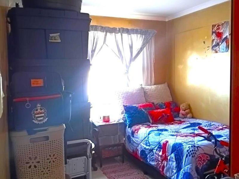 A compact bedroom featuring tiled flooring and a central ceiling light fixture, currently utilized with significant storage and personal items.