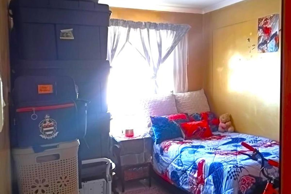 A compact bedroom featuring tiled flooring and a central ceiling light fixture, currently utilized with significant storage and personal items.