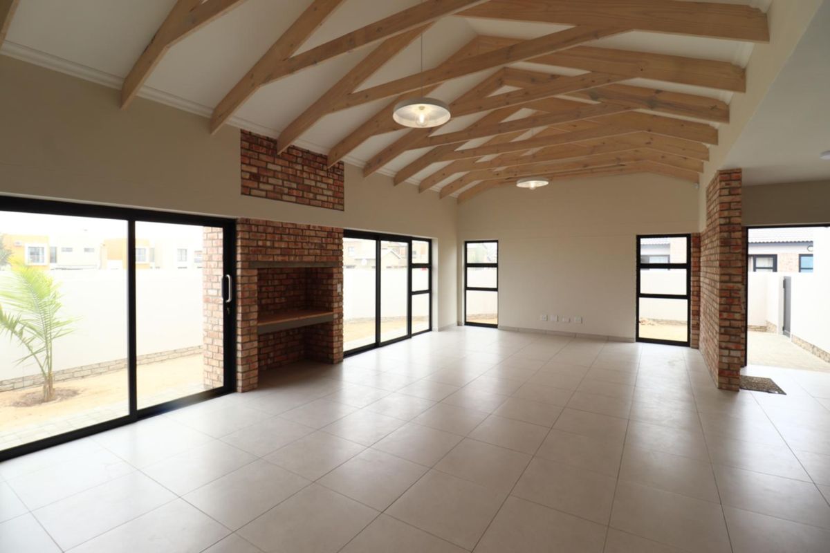 Spacious open-plan living area featuring exposed timber roof trusses, a brick fireplace, tiled flooring, and large sliding glass doors leading to the exterior.