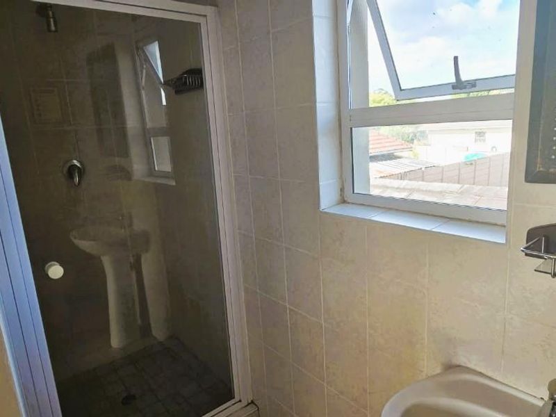 A functional bathroom featuring a shower enclosure, pedestal basin, and tiled walls, offering a clean and practical space with natural light.
