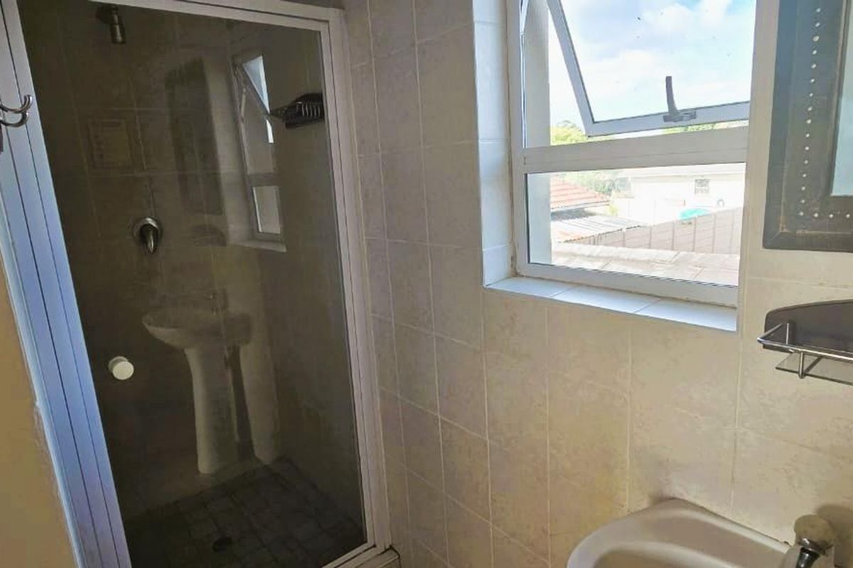 A functional bathroom featuring a shower enclosure, pedestal basin, and tiled walls, offering a clean and practical space with natural light.