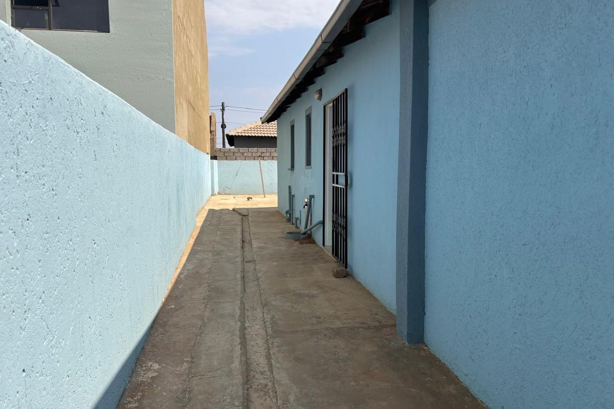 A side exterior walkway featuring concrete paving, a security gate, and blue painted boundary walls.
