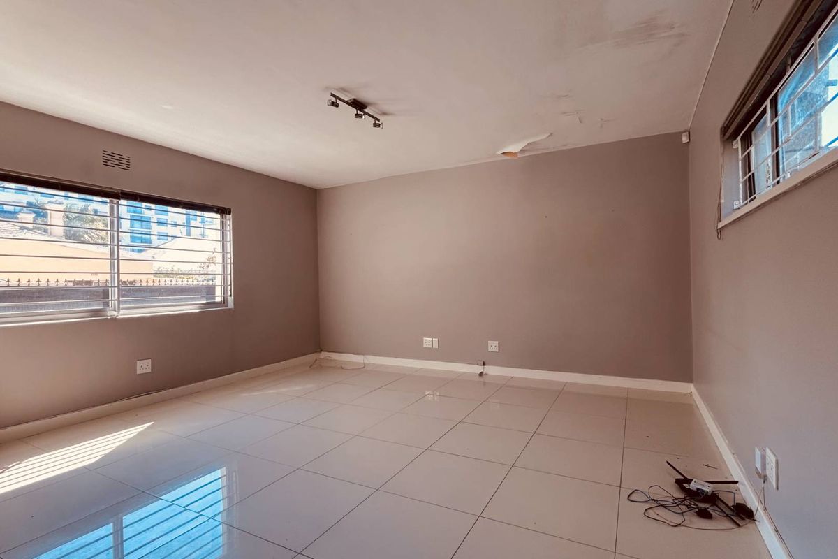 An empty living room featuring tiled flooring, security bars on windows, and ceiling-mounted lighting, requiring minor ceiling repairs.