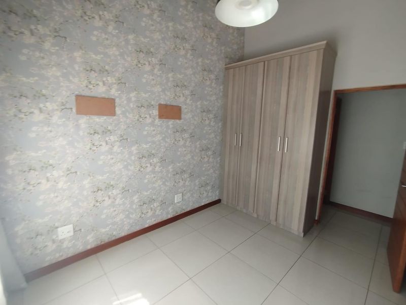 A bedroom featuring tiled flooring, a built-in wardrobe, and floral wallpaper, with visible wall patches requiring repair.