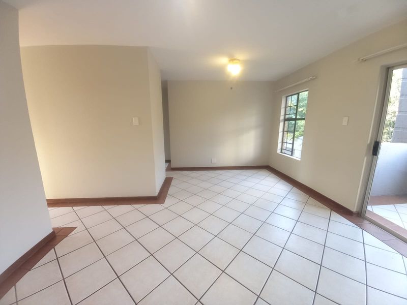 A bright, empty living area featuring neutral tiled flooring and a sliding glass door providing access to an outdoor space.