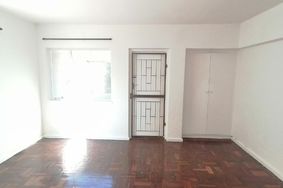 An empty bedroom featuring original parquet flooring, a built-in cupboard, and a security gate on the door.