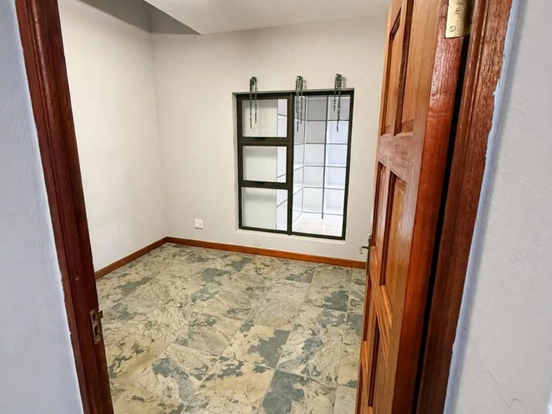 A vacant bedroom featuring tiled flooring, a timber door, and an aluminium-framed window, offering a clean and neutral space ready for personalization.