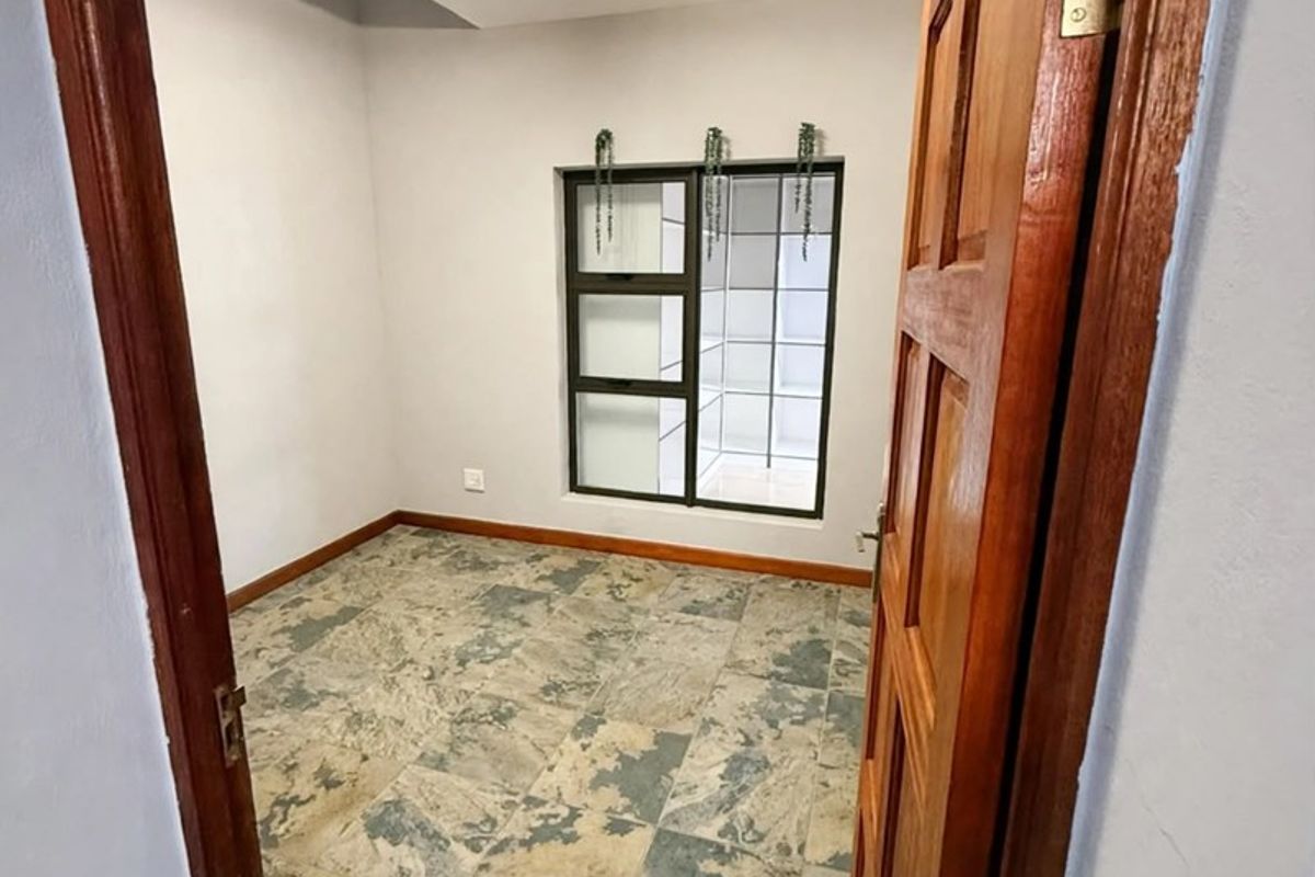 A vacant bedroom featuring tiled flooring, a timber door, and an aluminium-framed window, offering a clean and neutral space ready for personalization.