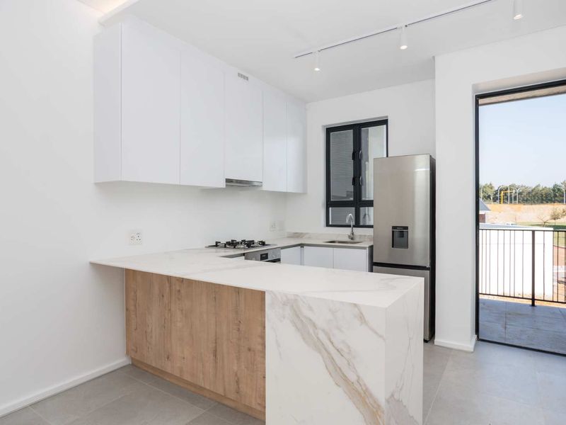 Modern kitchen featuring white cabinetry, stone countertops with a waterfall edge, gas hob, and integrated track lighting, with direct access to a balcony.