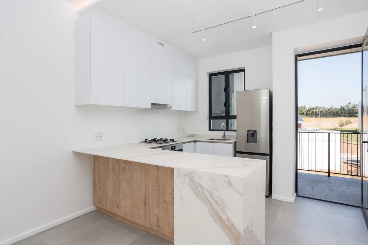 Modern kitchen featuring white cabinetry, stone countertops with a waterfall edge, gas hob, and integrated track lighting, with direct access to a balcony.