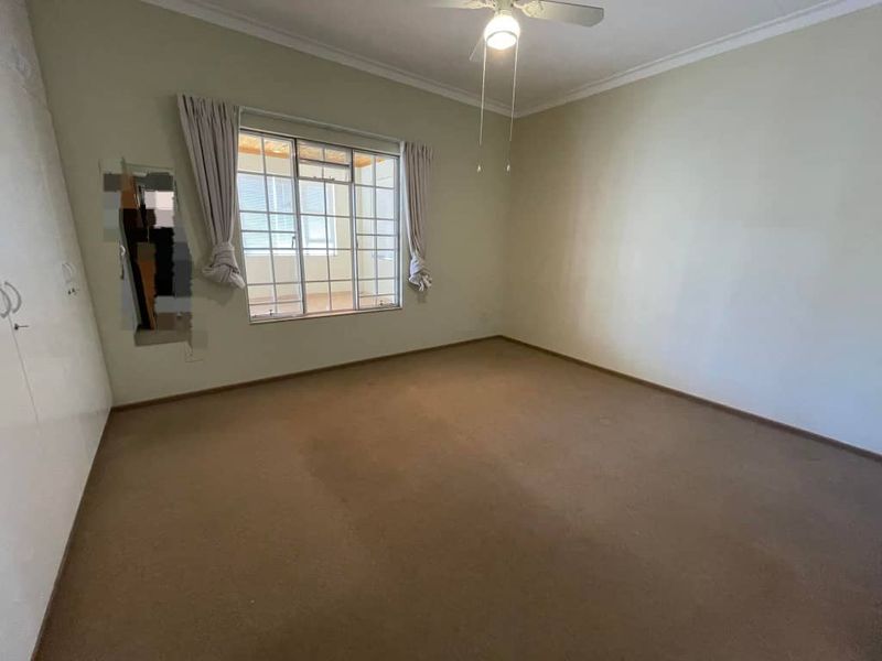 An empty bedroom featuring built-in cupboards, a ceiling fan, and carpeted flooring, requiring minor repairs to the wall and carpet.
