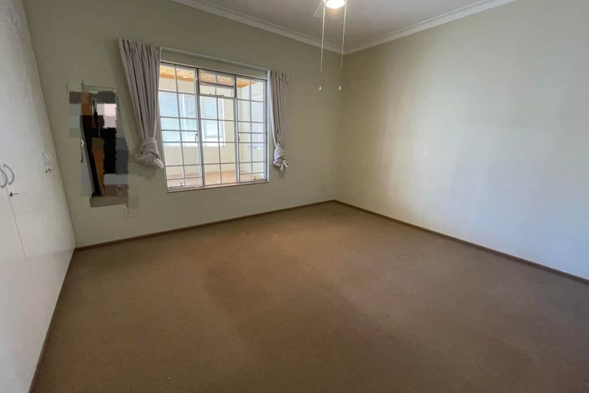 An empty bedroom featuring built-in cupboards, a ceiling fan, and carpeted flooring, requiring minor repairs to the wall and carpet.