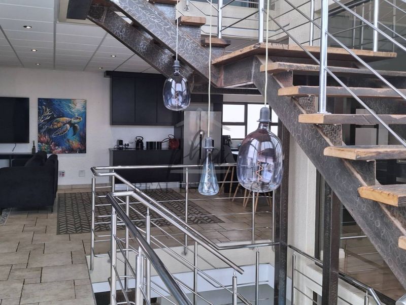 An open-plan living area featuring a striking open-tread staircase with stainless steel balustrades, tiled flooring, and modern recessed lighting.