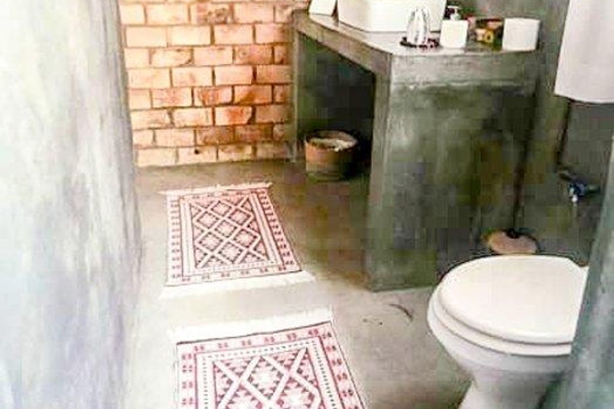 A rustic-style bathroom featuring an exposed brick wall, a concrete vanity with a vessel sink, and industrial-style exposed copper piping.