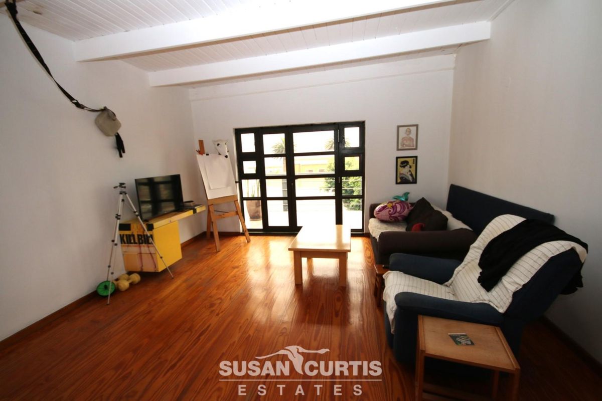 A living room featuring polished timber flooring, exposed white ceiling beams, and large glass-paned doors providing natural light and outdoor access.