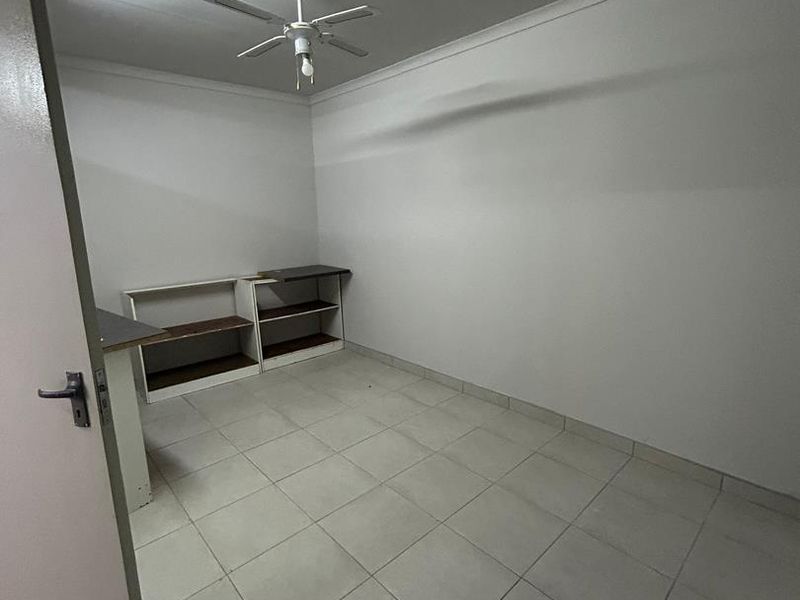 A clean, empty utility space featuring tiled flooring, a ceiling fan, and built-in shelving units, suitable for a home office or storage area.