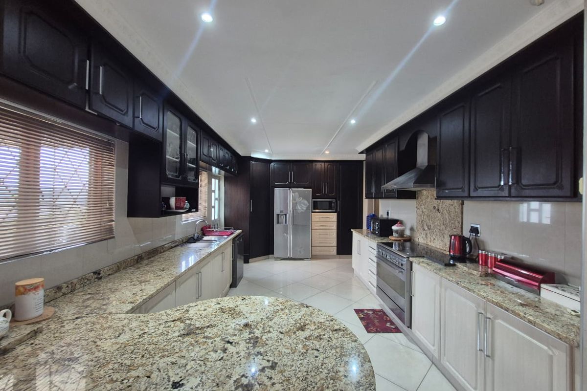 Spacious kitchen featuring granite countertops, a mix of dark and light cabinetry, built-in oven, extractor fan, and tiled flooring.