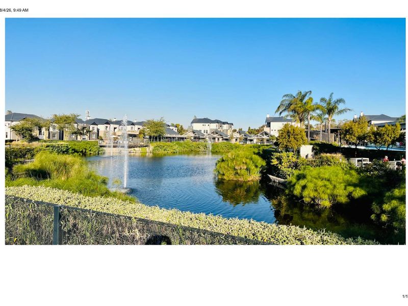 A scenic view of the apartment complex grounds featuring a central pond with water fountains and well-maintained landscaped gardens.