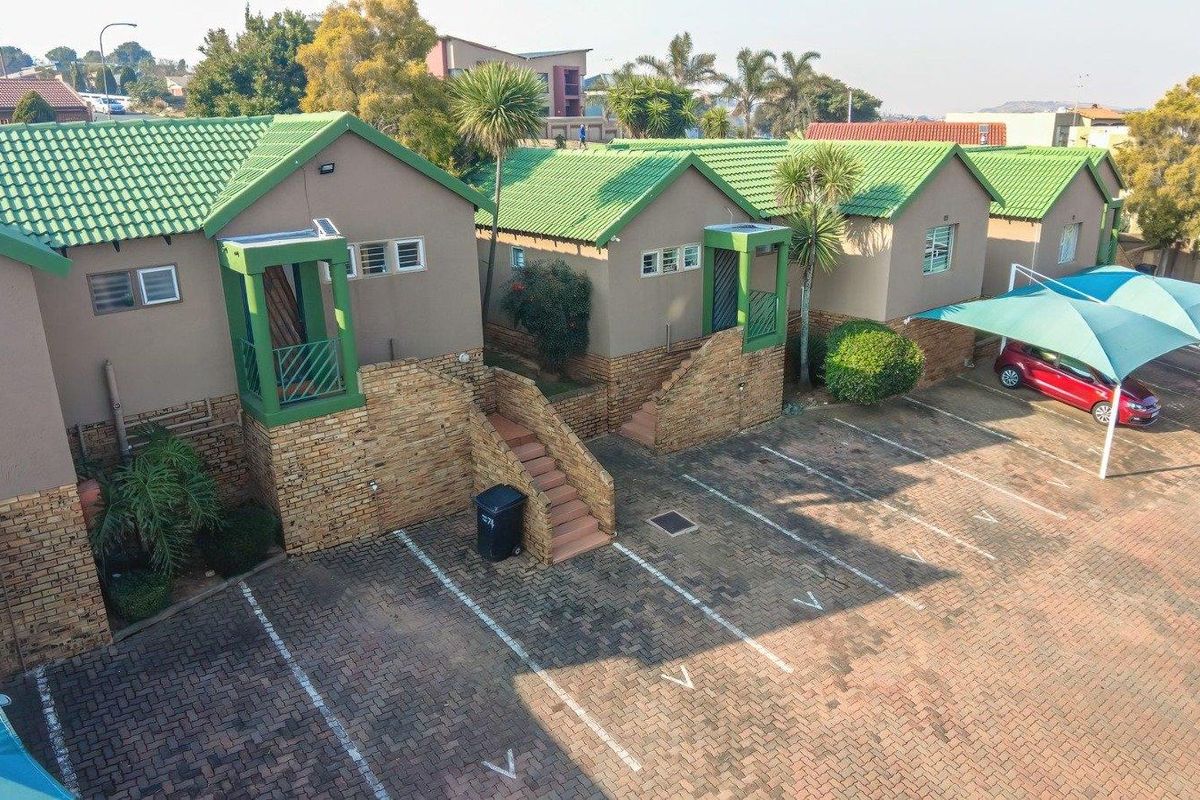 Aerial view of a townhouse complex featuring green tiled roofs, stone-clad facades, paved parking areas, and covered carports.