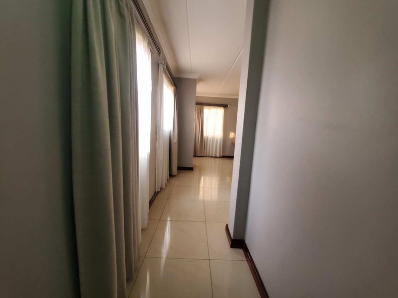 A bright, empty hallway featuring neutral tiled flooring, clean walls, and large windows with curtains, providing a spacious transition between living areas.